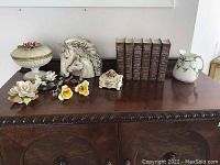 Overview of collection on wooden cabinet including porcelain and ceramic flower figurines, horse head sculptures, trinket boxes, and small pitcher