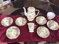 Full view of the tea set including teapot, six teacups with saucers and creamer, displayed on a burgundy cloth.