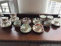 Eight teacup and saucer sets displayed on wood surface under window