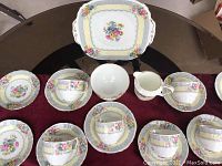 Full set of china including serving dish, cream pitcher, bowl, four teacups and saucers laid out on table.