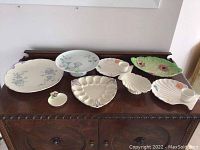 Overhead view of all 8 pieces arranged on a wooden surface showing various ceramic serving and plate items with floral patterns and pastel colors.