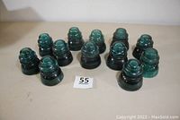 12 Hemingray-42 glass insulators in green-blue on table, visible chips and wear on some.