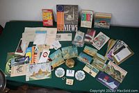 Overview of entire lot on green cloth: Unisphere bank, ashtrays, guides, brochures, postcards, flash cards and novelty key purse