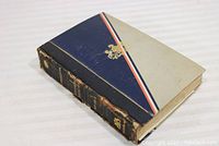 Front cover of the antiquarian book showing tri-color design and gold emblem with visible wear.