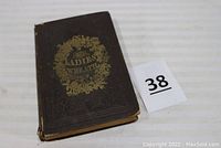 Photo of front cover showing brown hardcover with embossed and gold lettering 'The Ladies Wreath' surrounded by floral design.