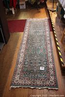 Full length view of the blue-green oriental runner rug placed on wooden floor showing floral design and fringe ends.