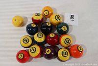 Top view photo showing all 16 billiard balls arranged in a cluster with a small paper label numbered 8 next to them.
