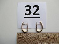 Pair of gold pierced earrings laid side by side above a ruler showing approximately 1 inch length each.