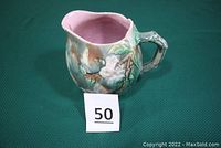 Side view of the Etruscan Majolica milk pitcher showing the twig handle, floral relief pattern, and mottled finish.