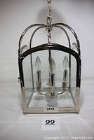 Front view of square lantern style chandelier showing polished metal frame, glass panels, four candle shaped bulbs and hanging chain.