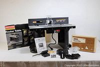 Craftsman router table fully assembled on a table with original box, manuals, and multiple accessories laid out in front.