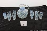 Full set photograph showing the opalescent pitcher surrounded by 10 matching drinking glasses arranged on a flat surface with a label '3' in front