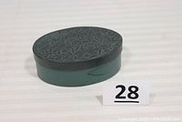 Side view of oval bentwood shaker box with dark outer band and textured lid, placed beside lot number card 28.
