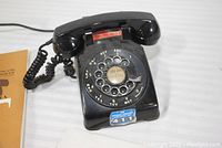 Black rotary dial telephone with visible rotary dial and handset, showing area code 215 on the dial.