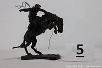 Side view of bronze statue showing cowboy with lasso on bucking horse with identification number marker