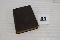 Closed brown hardback book with wear to edges and corners, placed on a white surface with lot number 39 nearby.