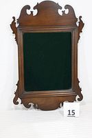 Front view of the mirror showing the full frame with intricate carved scrolls and solid mahogany finish against a white background with a green cloth inside the reflection area.