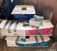 Stacked boxes containing two artificial Christmas trees and other holiday items.