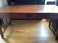 Front view of wood desk showing surface, drawer, and side slatted panel design.