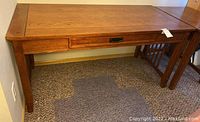Full frontal image of the wooden desk showing the tabletop and legs, highlighting the wood grain and drawer placement.