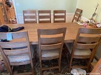 Eight wooden ladder-back dining chairs around a wooden table, showing overall condition and style.