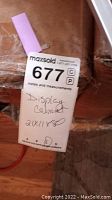 Photo of label on the packaging showing 'Display Cabinet 21x11x80' with MaxSold lot tag and code 677 C P