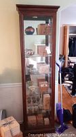 Front view of tall wooden display cabinet showing crown molding top, glass door, and four glass shelves with lighting