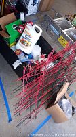 Photo showing assorted gardening chemicals, red metal tomato cages, and other garden supplies in plastic bin, ladder and boxes in background
