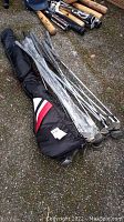 Full view of golf clubs in the black carry bag lying on pavement alongside baseball bats.