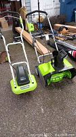 Full view of two Greenworks electric lawn tools side by side on pavement, showing handles and bodies.