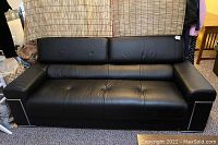 Front view of three-seat black leather sofa with tufted seats and silver trim