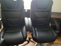 Front view of two black leather office chairs with cushioned backs and arm rests positioned next to each other.