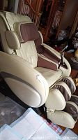 Overall front-side view of the cream and brown Osaki massage chair showing headrest, armrests, and footrest