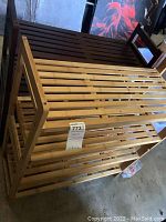 Photo showing one brown wooden shoe rack with three slatted shelves behind two bamboo wooden shoe racks.