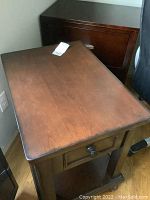 Top view of rectangular dark wood side table showing surface wear and scratches, one drawer visible with round knob.