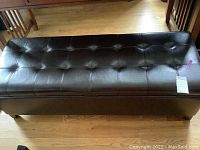 Image showing the full closed leather bench with tufted top and tag attached.
