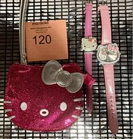 Two Hello Kitty wristwatches with a pink glitter Hello Kitty face wristlet purse on a black metal grid surface with auction lot sticker visible.