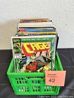 Green basket full of assorted comic books with visible front cover showing 'Cage' Marvel comic book