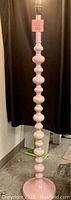 Full view of tall floor lamp showing stacked curvy bulbous segments in soft pink lacquer finish under a light bulb socket.