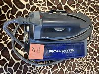 Full view of Rowenta Expert steam iron placed on its base with blue water reservoir and braided steam hose, showing cord and brand label.