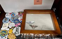 Wooden shadowbox frame with etched 'FRIENDS' glass top and assorted vintage pins arranged beside it