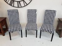 Front view of three buffalo plaid upholstered dining chairs with black legs against a wall