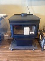 Front view showing stove body, ceramic glass door with label, pedestal base on display platform