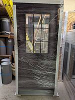 Steel entry door system wrapped in plastic showing slab, glass grid, frame and sill.
