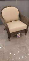Front angled view of wicker armchair with beige cushions in showroom