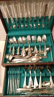 Full view of wooden flatware case with multiple rows of silver plated knives, forks, spoons