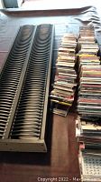 Photo showing two black plastic curved CD storage racks and multiple stacks of CDs in jewel cases on a table.