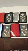 Overview of four proof sets in original cases showing red and blue covers, interior foam trays and certificates.