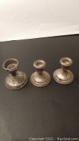 Three silver sterling candle stick holders showing tarnish and decorative rim details.