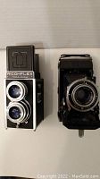 Two vintage cameras side by side: Ricohflex Holiday twin-lens reflex on left and Zeiss Ikon folding camera on right